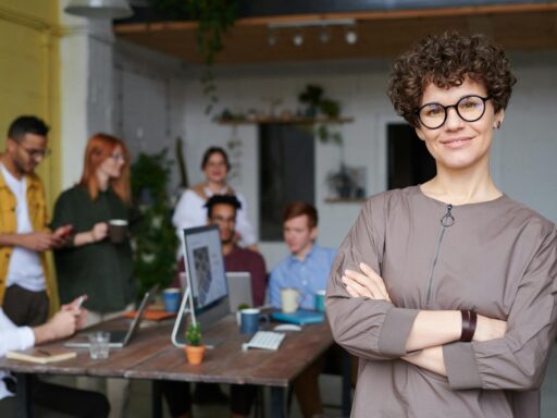 Smiling businesswoman with curly hair stands confidently in a modern office space with colleagues.