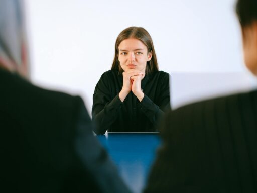 A woman in a job interview facing two people at an office table, focusing intently.