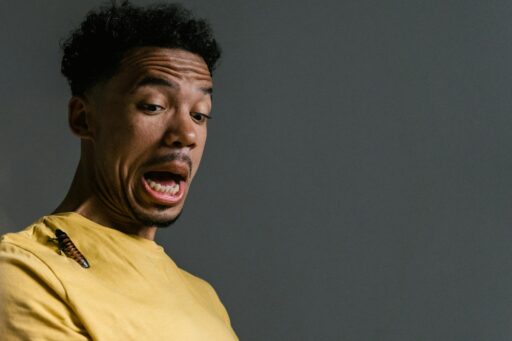 A startled man expresses fear as a cockroach sits on his yellow shirt, capturing a moment of surprise and anxiety.