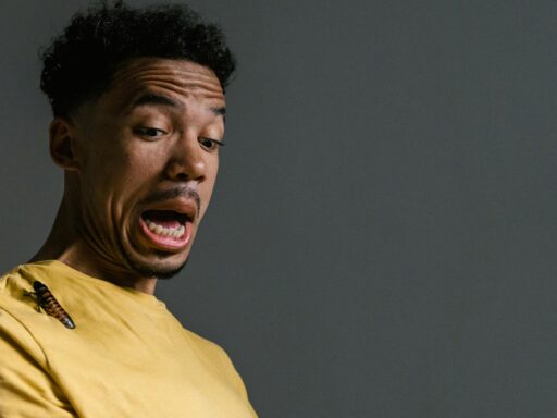 A startled man expresses fear as a cockroach sits on his yellow shirt, capturing a moment of surprise and anxiety.