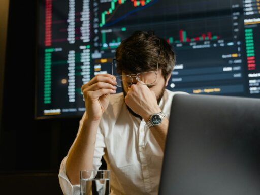 A stressed man looks at stock market data on his computer screen in an office setting.