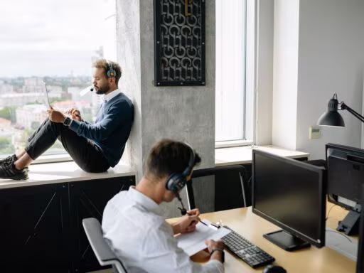 Two call center agents working in a modern office, one seated at a computer and another using a tablet by the window.